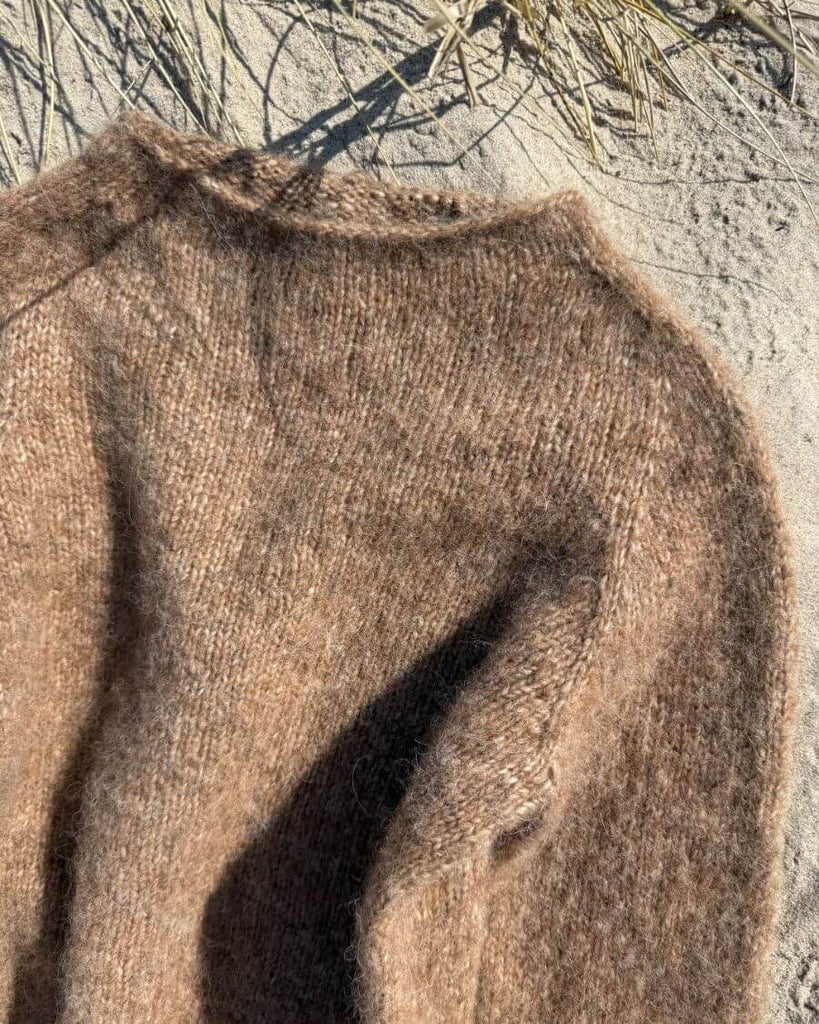 Detaljebillede af halsen på brun Ivy Sweater liggende i sandet