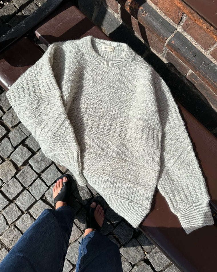 Lysegrå Storm Sweater liggende på sand