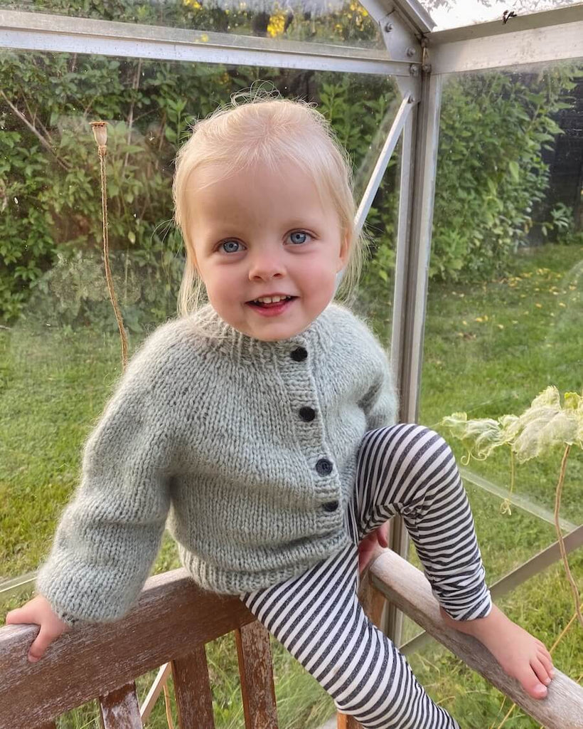 Barn iført lysegrøn Novice Cardigan Mini – Chunky Edition